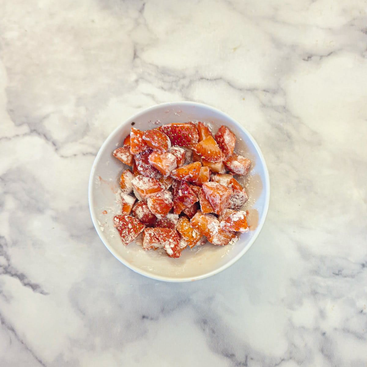 Chopped strawberries lightly coated in flour in a small white dish.