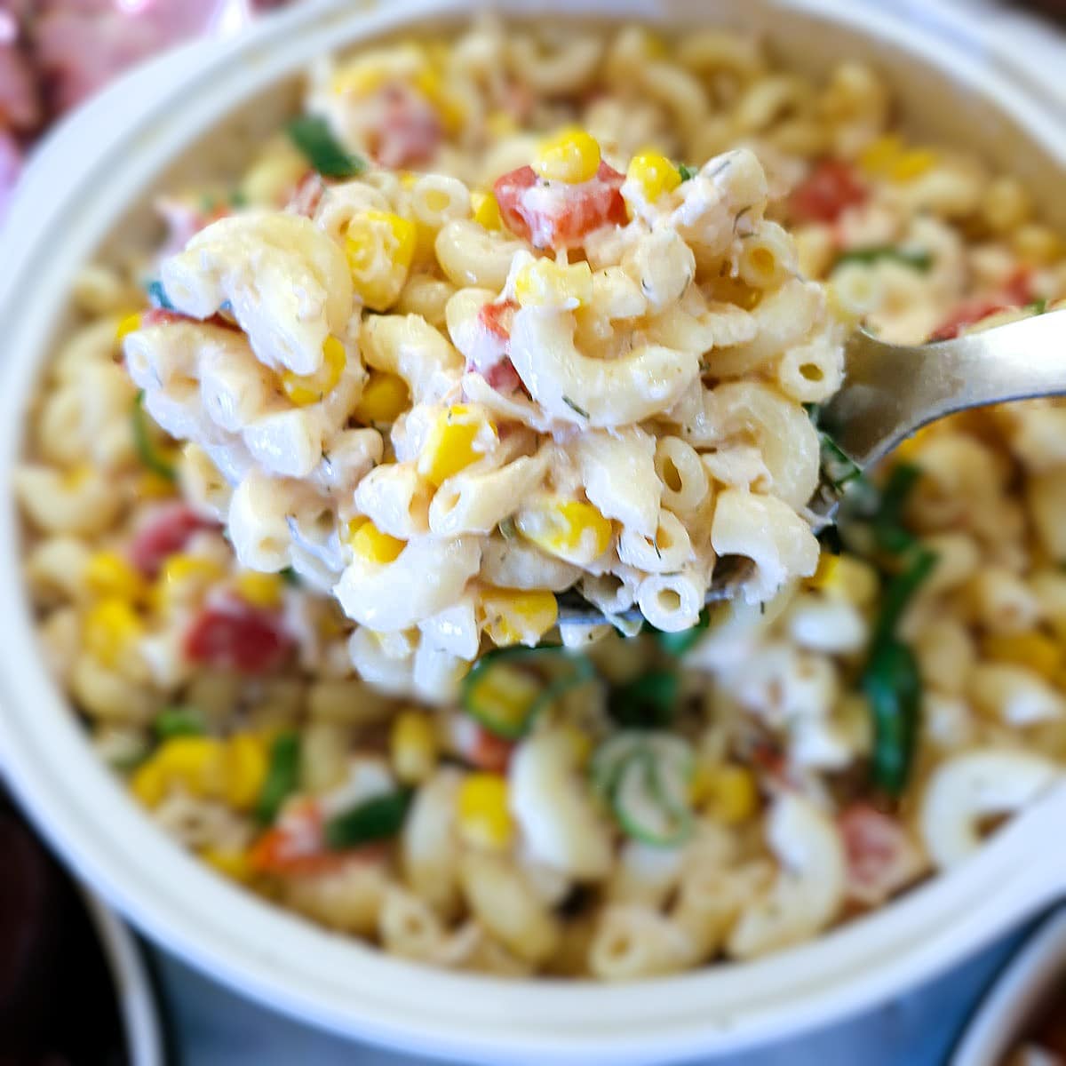 A spoonful of crab and roasted pepper pasta salad being lifted from a serving bowl.