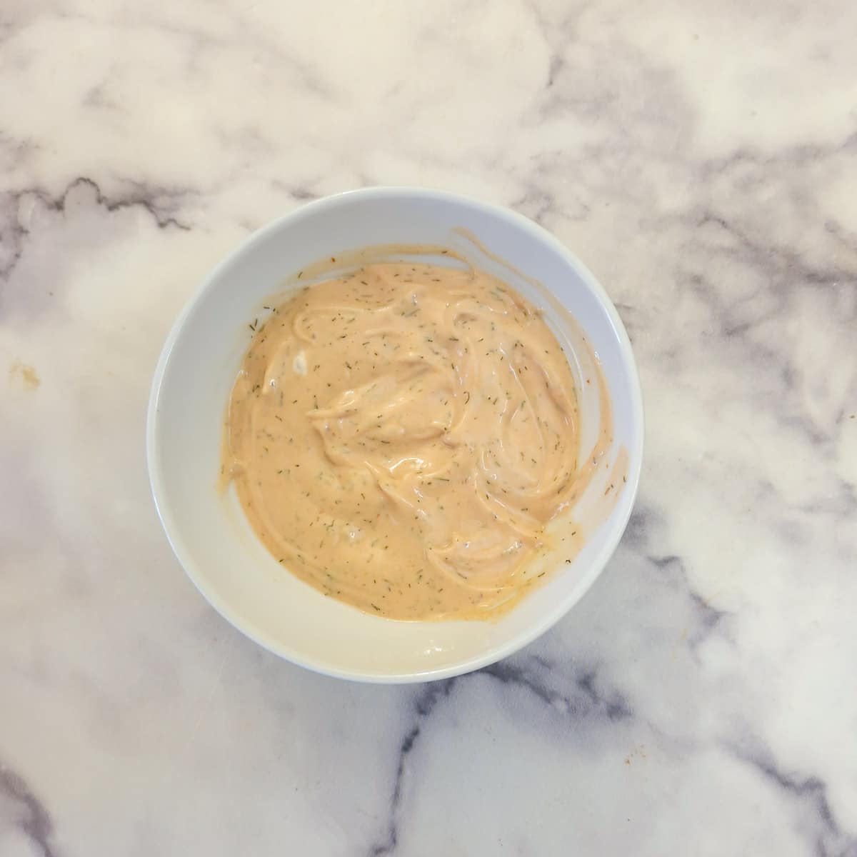Marie Rose sauce combined with driied dill in a small white bowl.