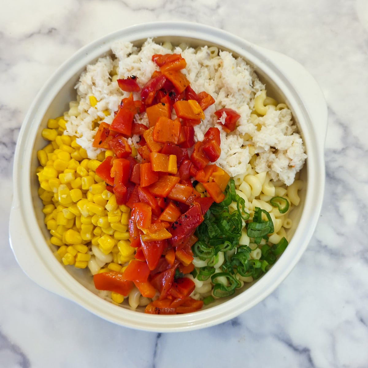 Red peppers, green onions, crab and sweetcorn on top of noodles in a serving bowl.