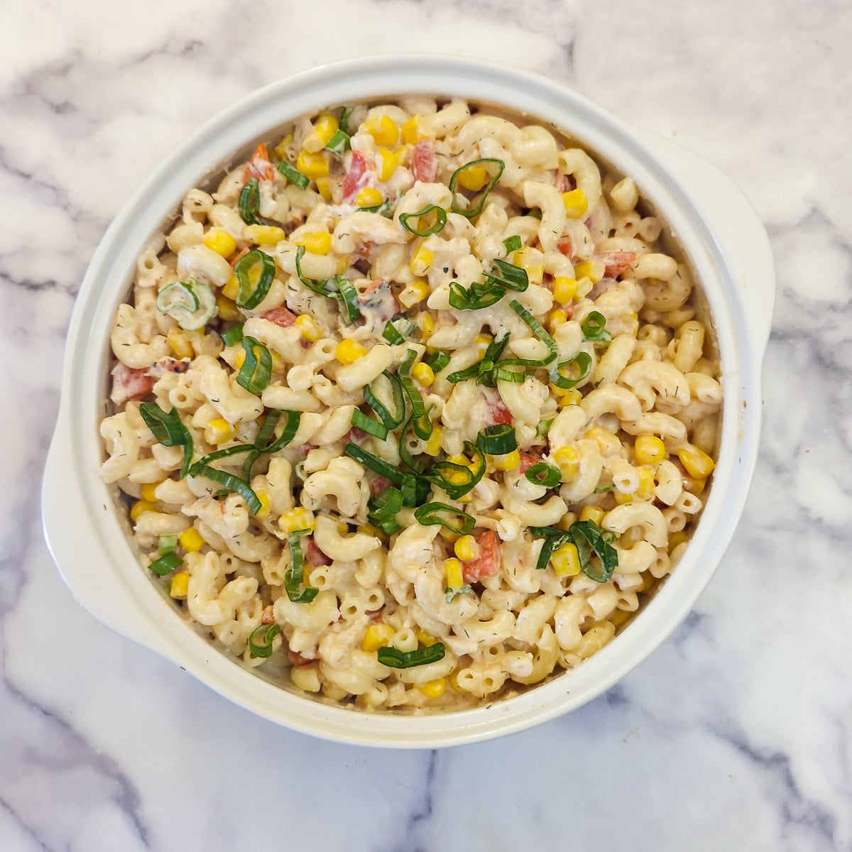 A prepared crab and roasted pepper pasta salad in a white serving bowl garnished with chopped spring onions.