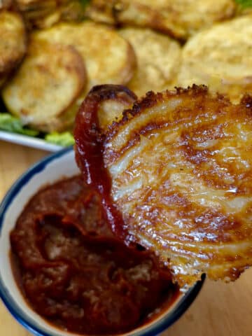 A cheesy potato and onion slice being dipped into a bowl of tomato ketchup.