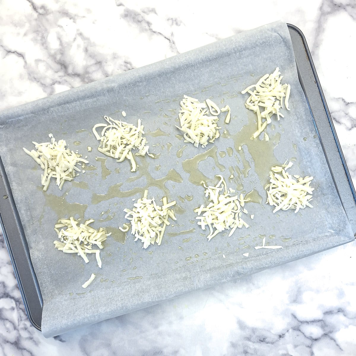 8 small mounds of grated cheese on a baking tray.