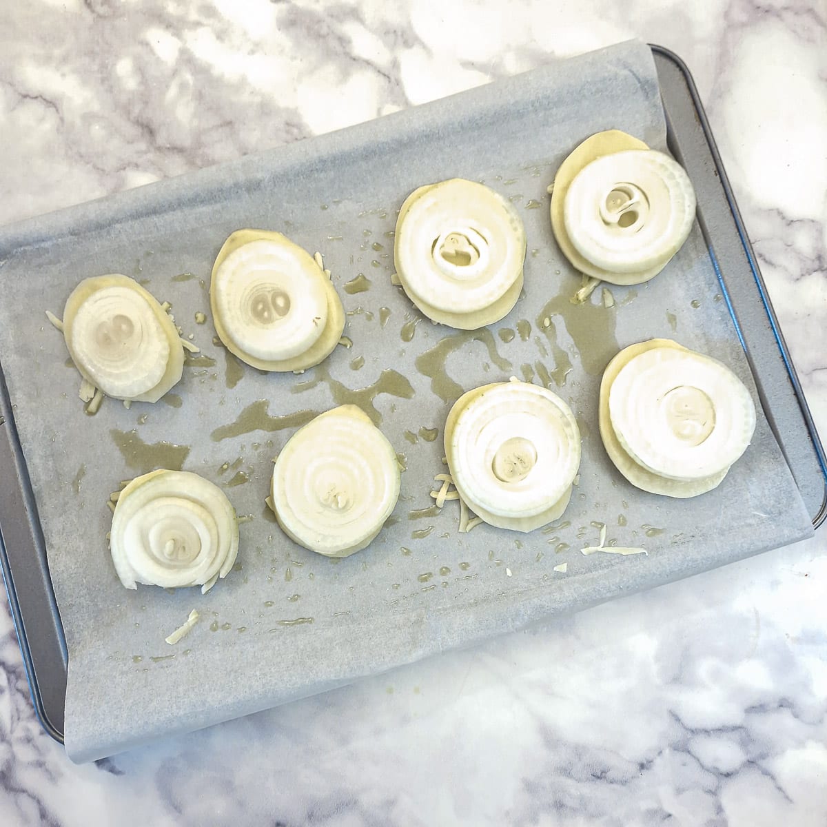 8 slices of potato and onion arranged on top of cheese on a baking sheet.