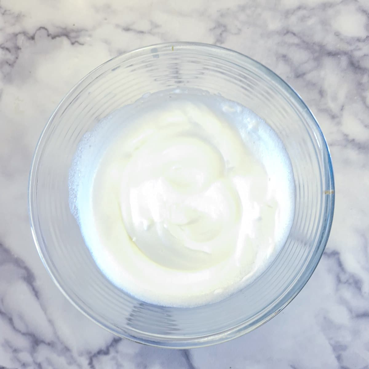 Egg whites whipped to soft peaks in a glass mixing bowl.