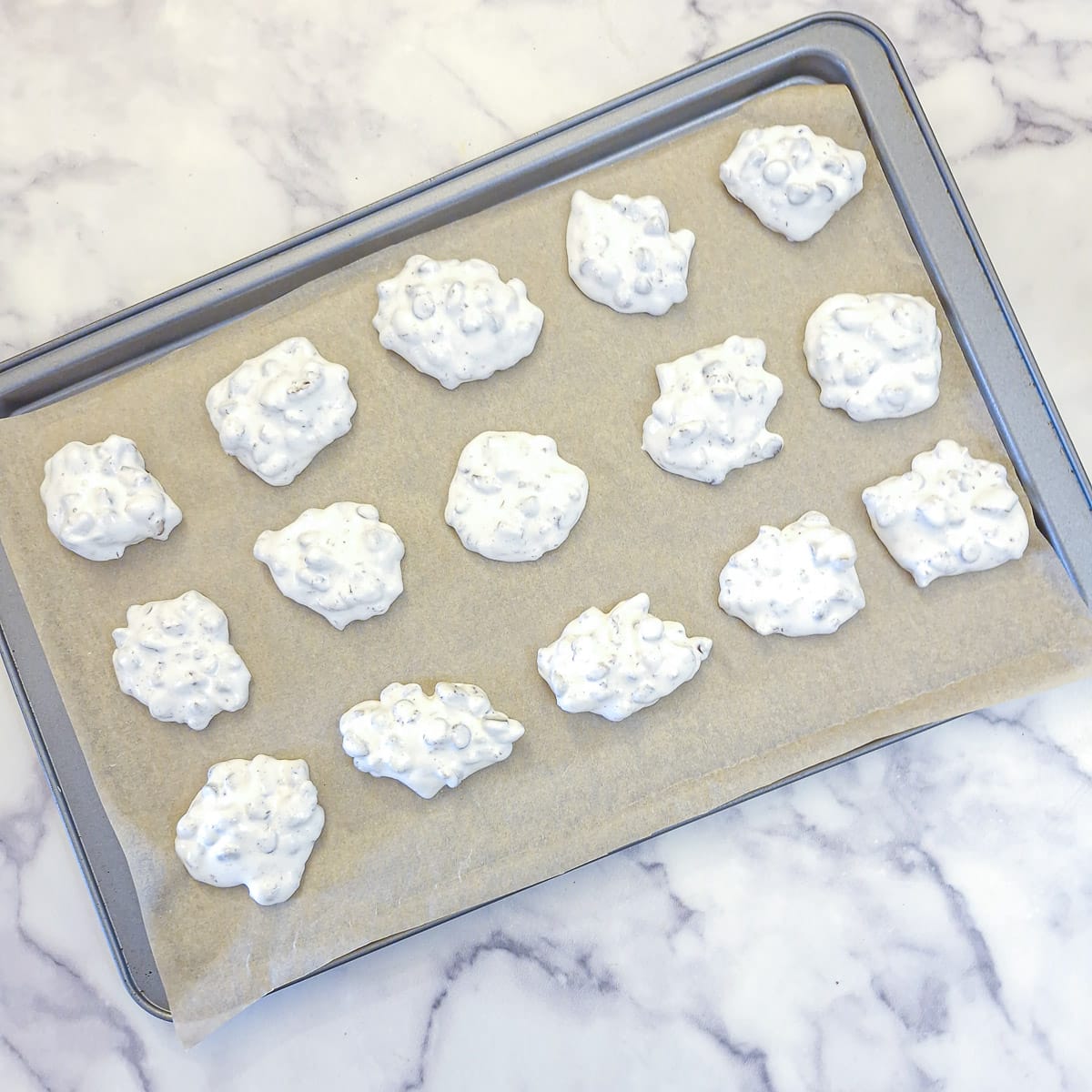 15 undried meringue nut cookies on a baking tray.