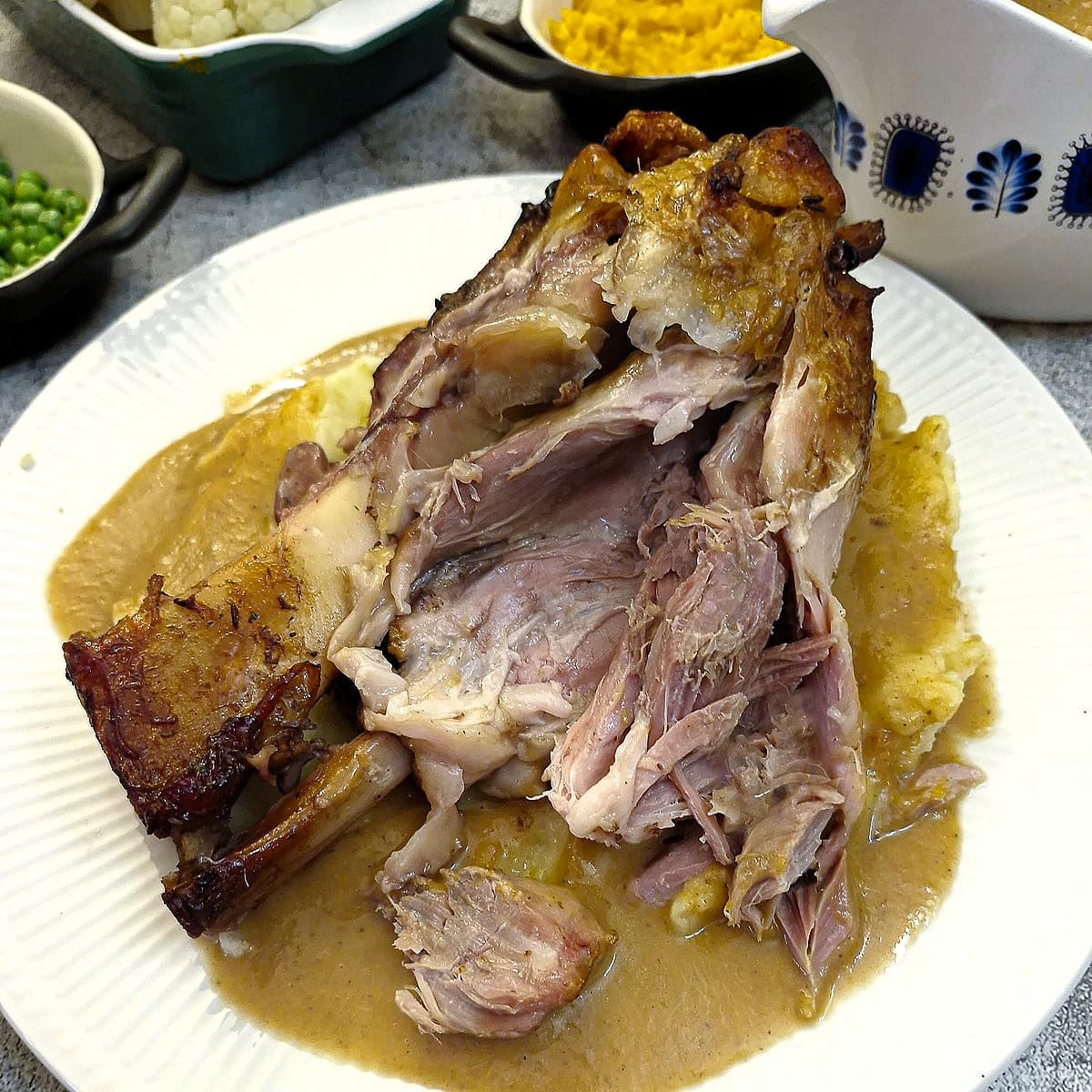 A cooked pork hock on white plate, with the hock cut open to show the tender meat inside.