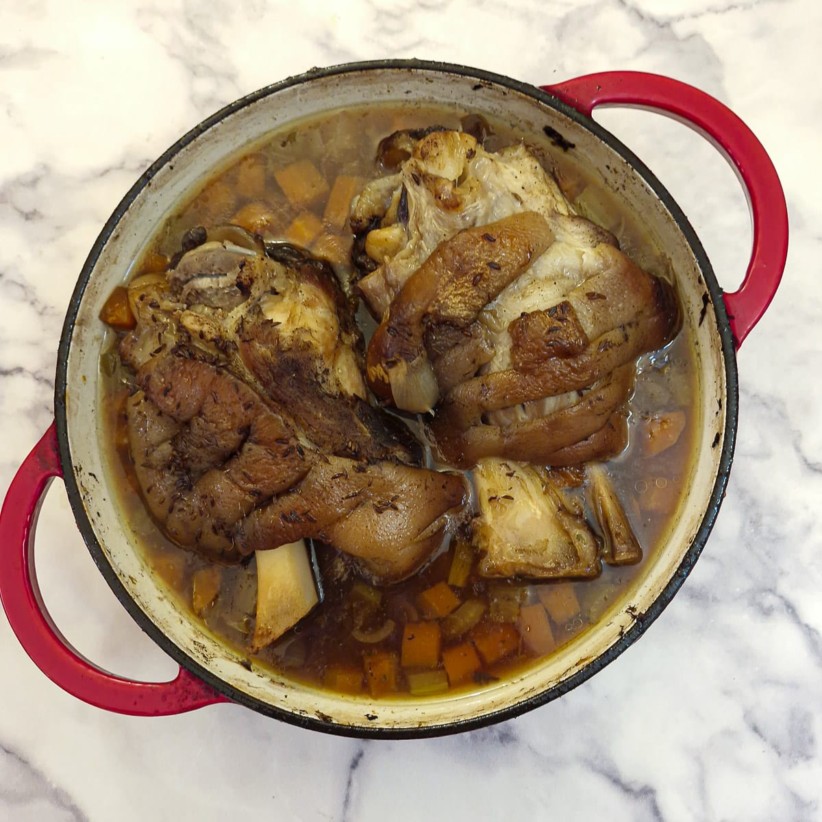 Two pork hocks in a dutch oven that have been fully cooked but not yet crisped.