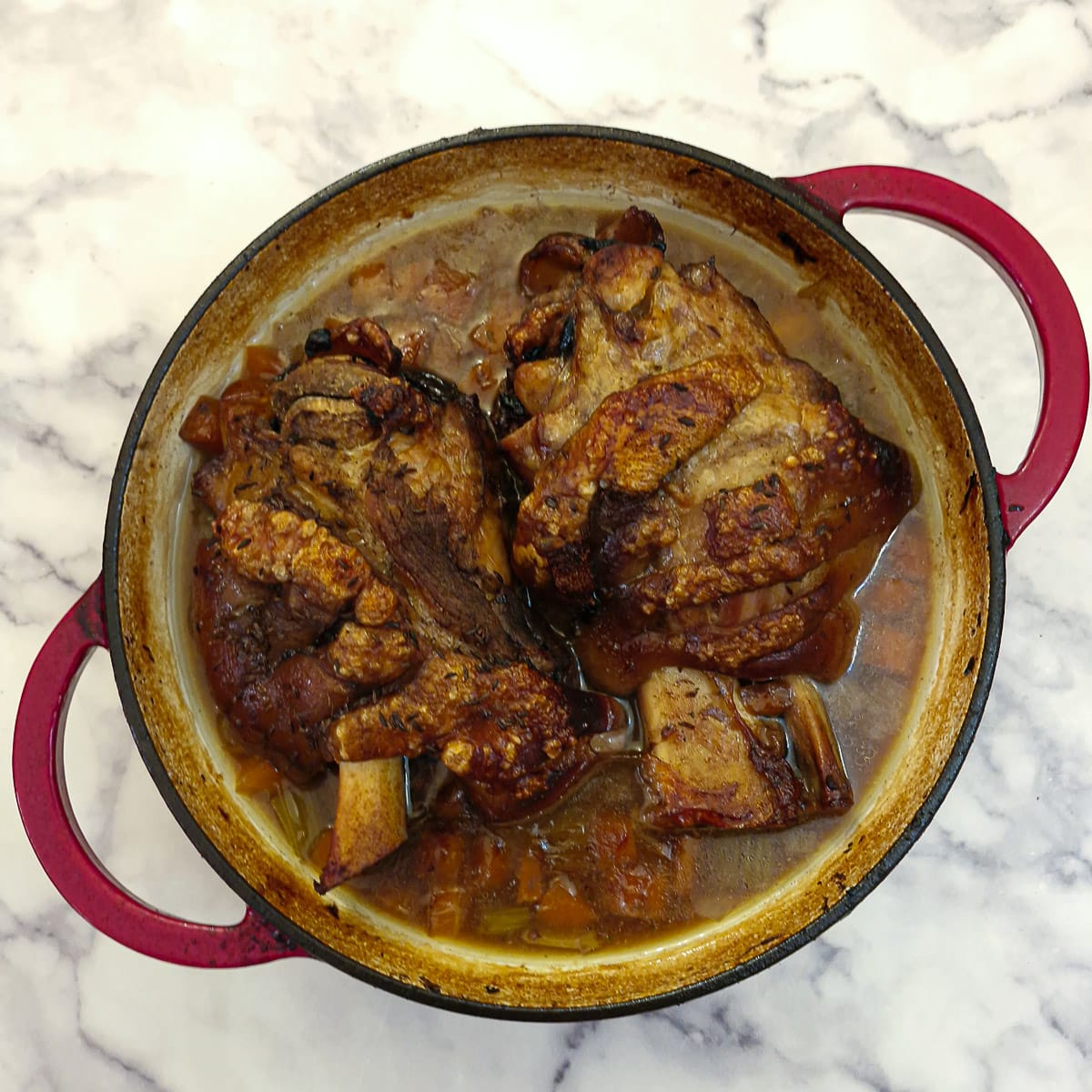 Two crispy pork hocks in a dutch oven.