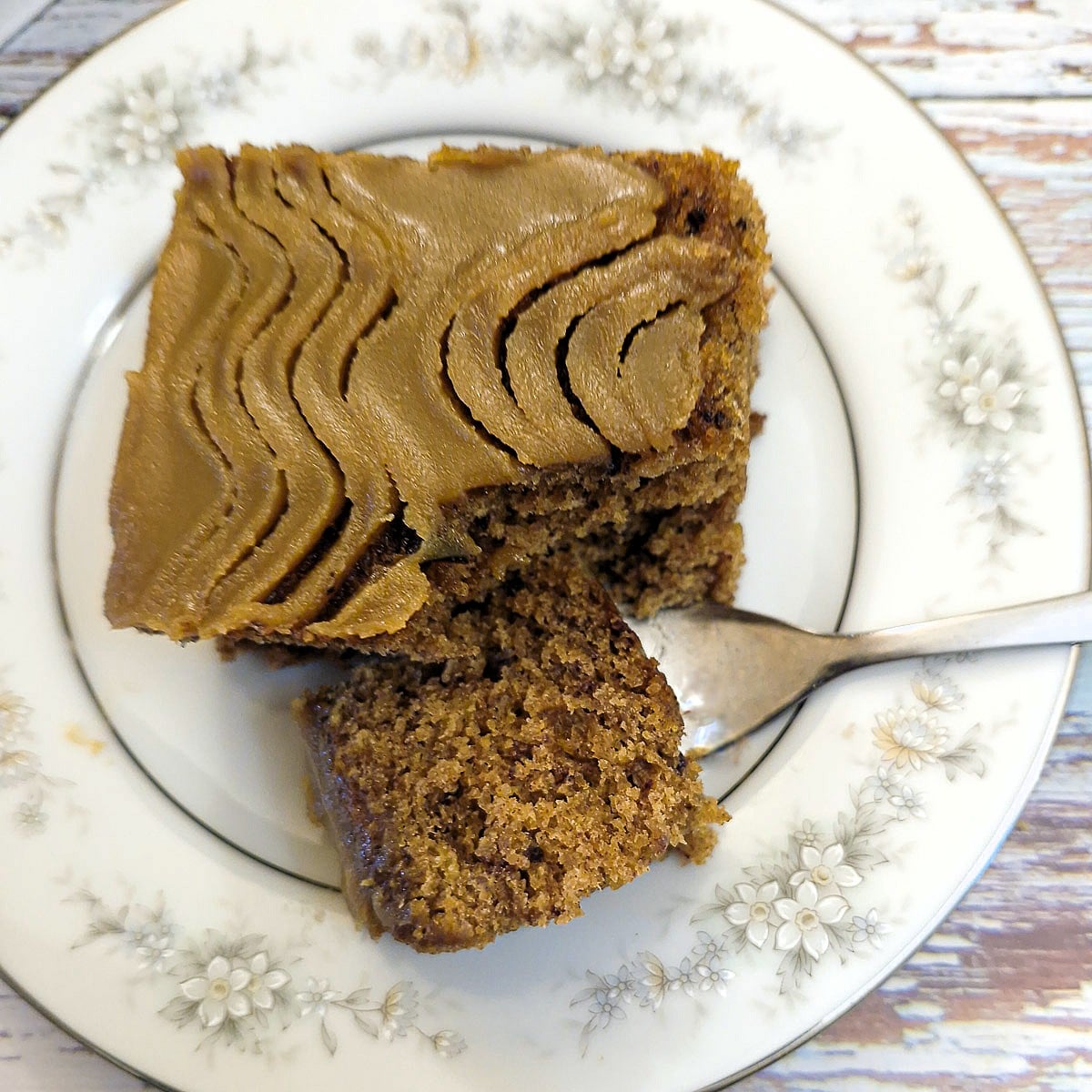 Overhead shot of a slice of sticky toffee pudding traybake cake on a blue patterned plate with a piece of cake on a fork.