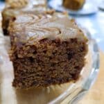 A slice of sticky toffee pudding traybake with toffee sauce glaze on a glass serving platter.