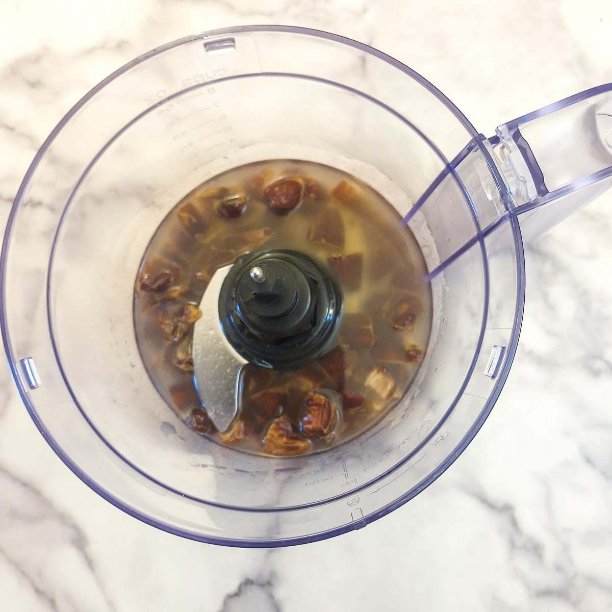 Chopped dates softening in water in the bowl of a food processor.