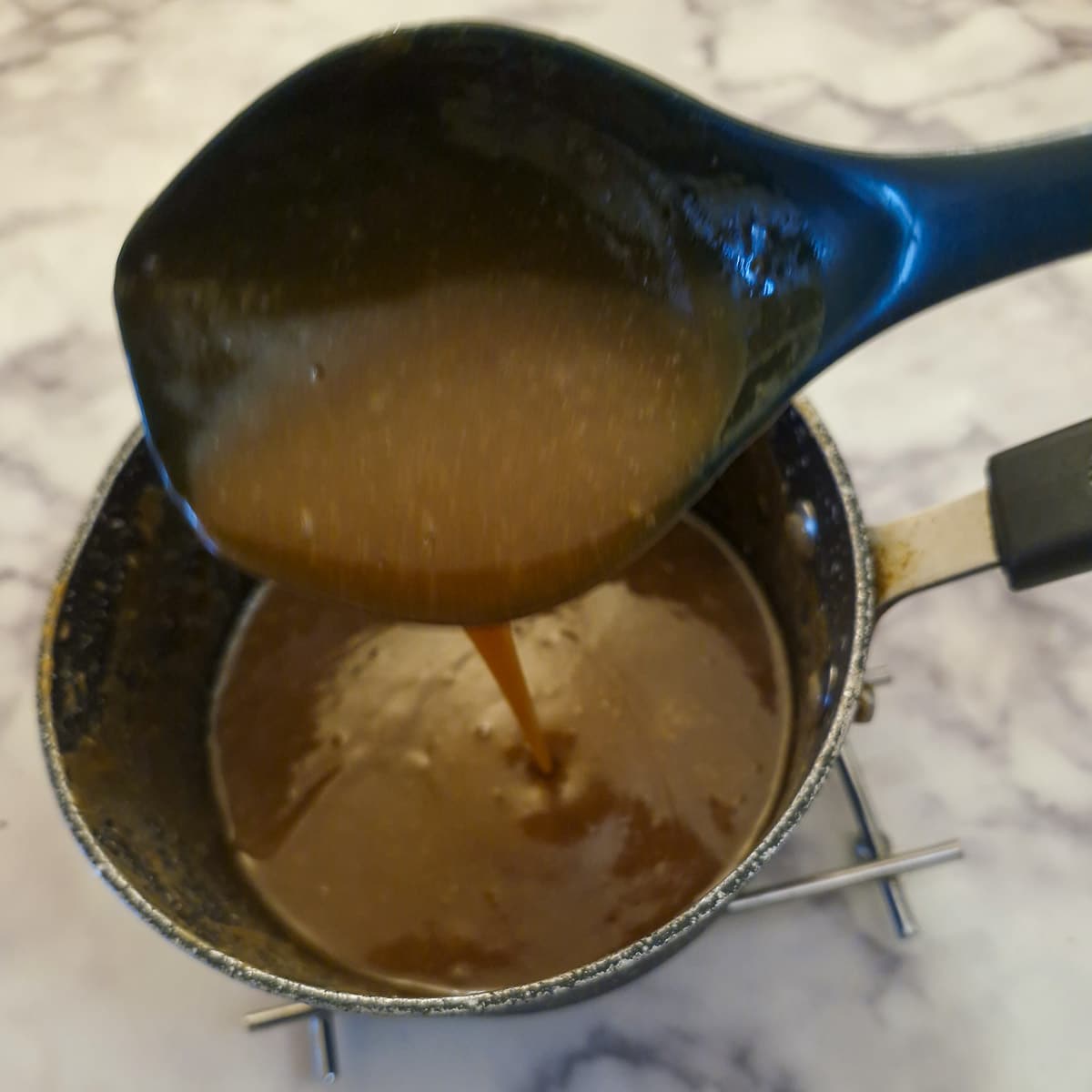 Toffee sauce being mixed in a saucepn with a spoonful of sauce being lifted from the pan.