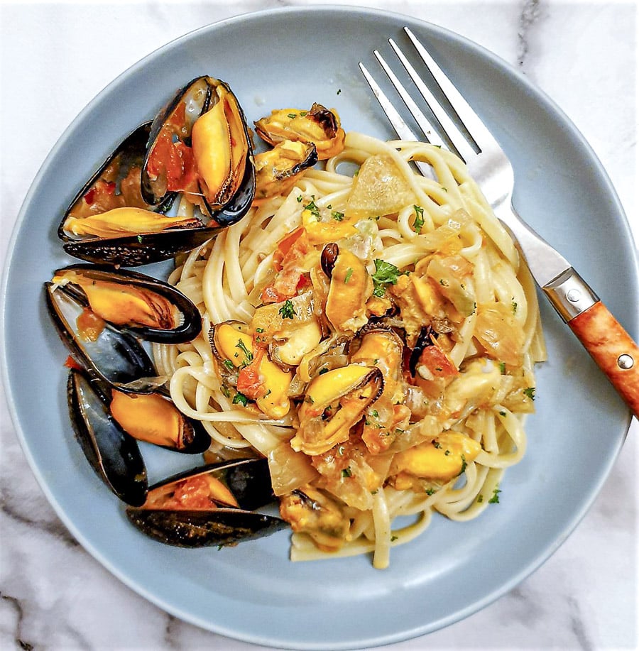 A plate of mussels with pasta, garnished with mussels in their shells.