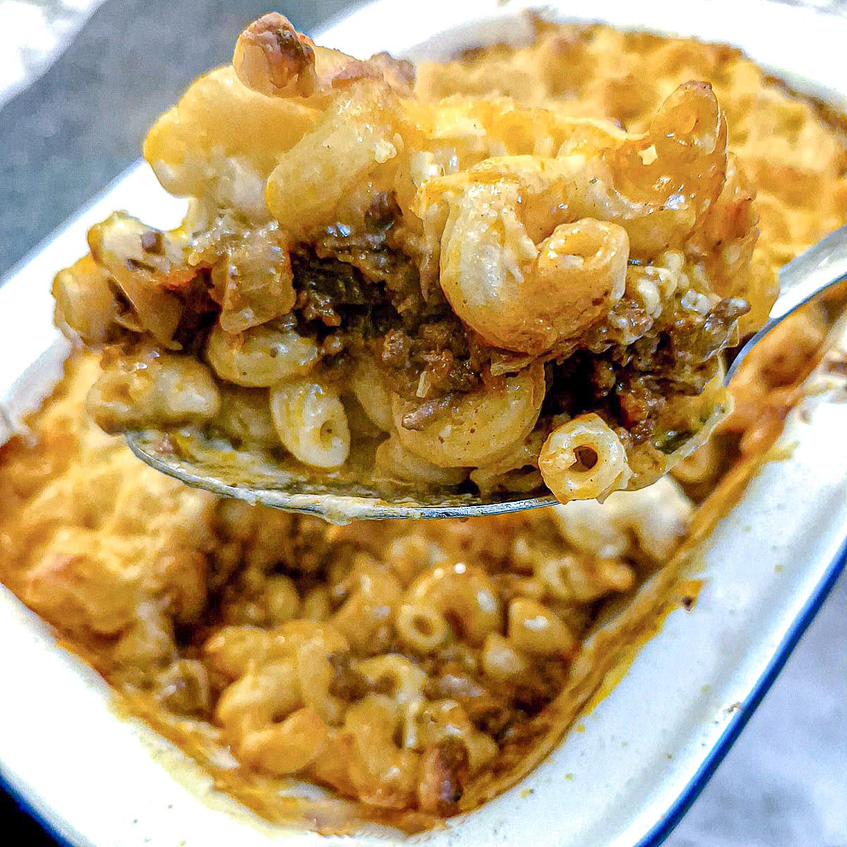 A spoonful of macaroni cheese lasagne being lifted from a serving dish.