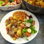 A white dinner plate with minced beef hash, baked beans and a side of green salad.