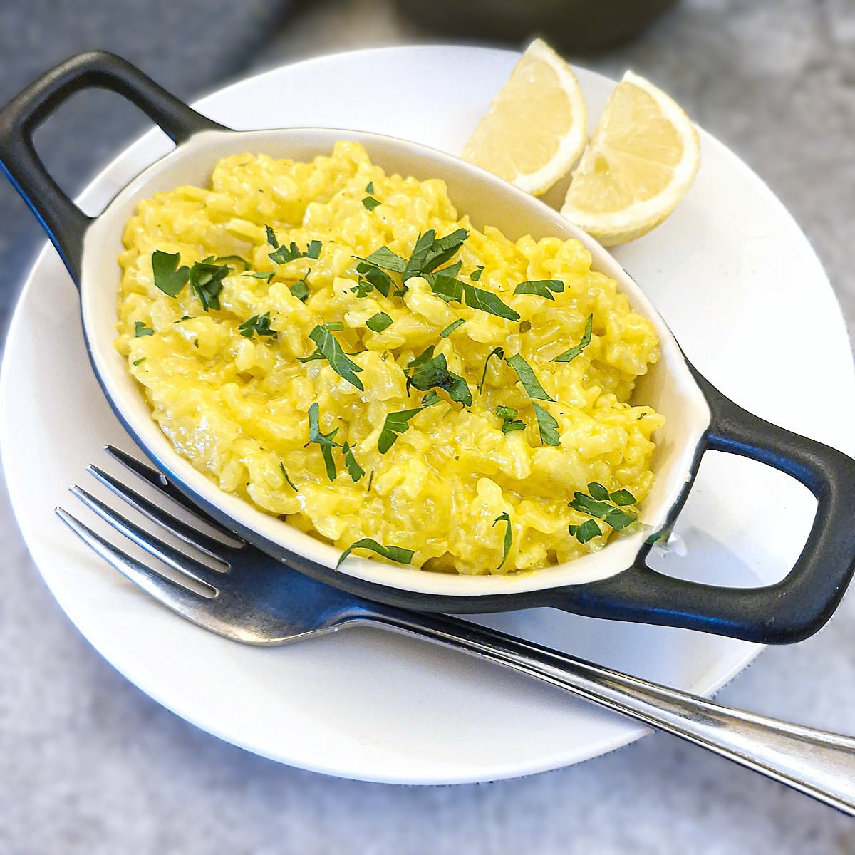 Overhead shot of a dish of risotto alla Milanese garnished with parsley and slices of lemon on the side.
