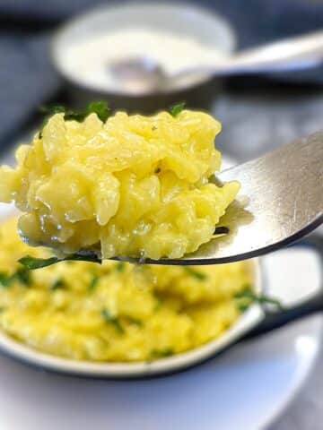 A forkful of risotto alla Milanese being lifted from a serving dish.