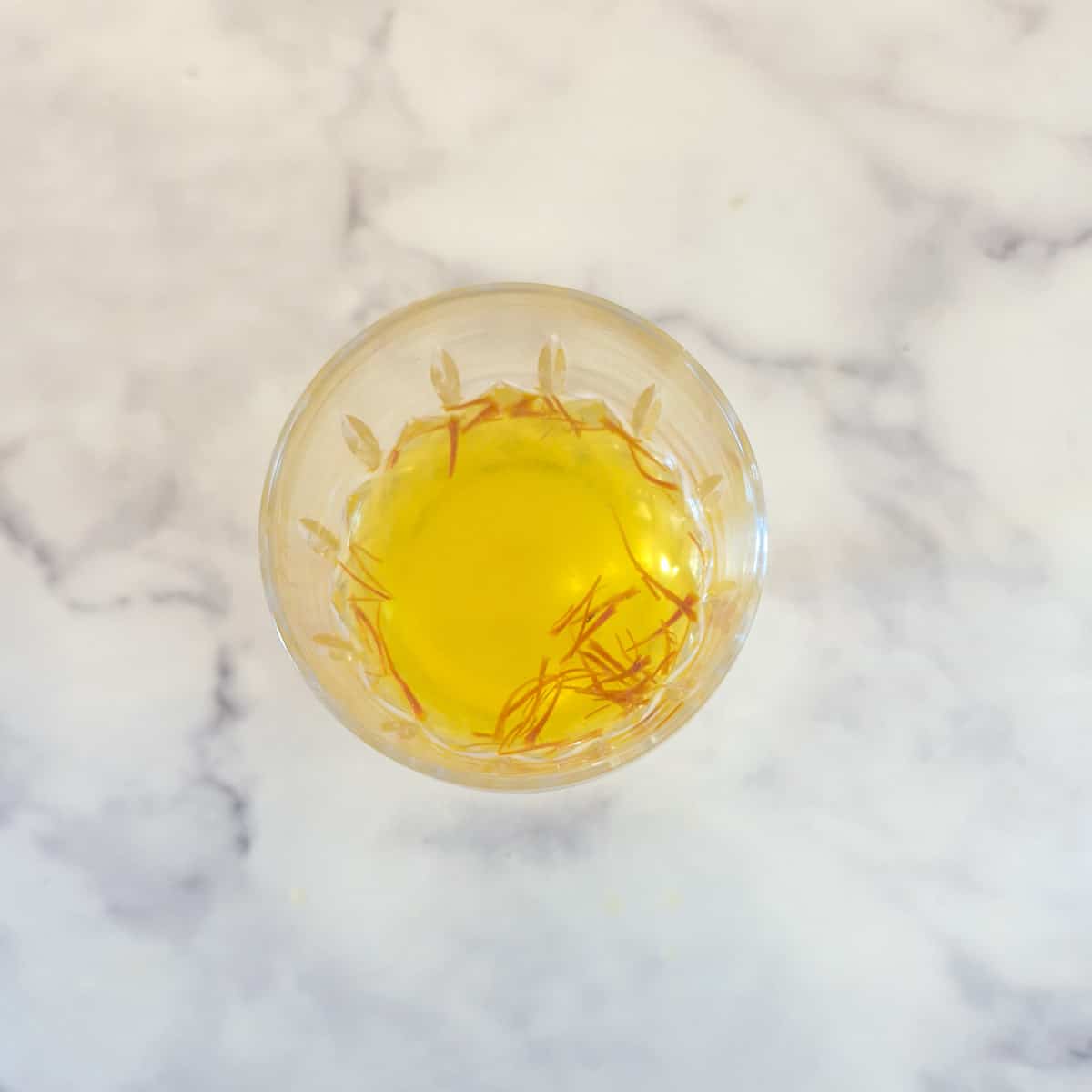 Saffron threads soaking in a mixture of vinegar and vinegar in a wine glass.
