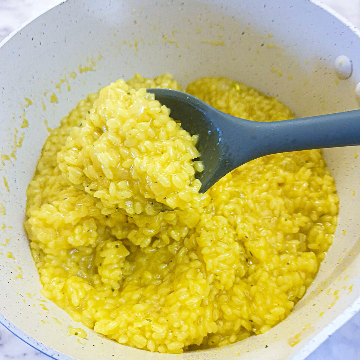 Parmesan cheese and butter stirred into the risotto alla Milanese in a saucepan.