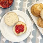 A cream scone cut in half, spread with butter and topped with strawberry compote.