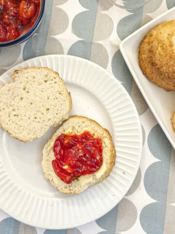 A cream scone cut in half, spread with butter and topped with strawberry compote.