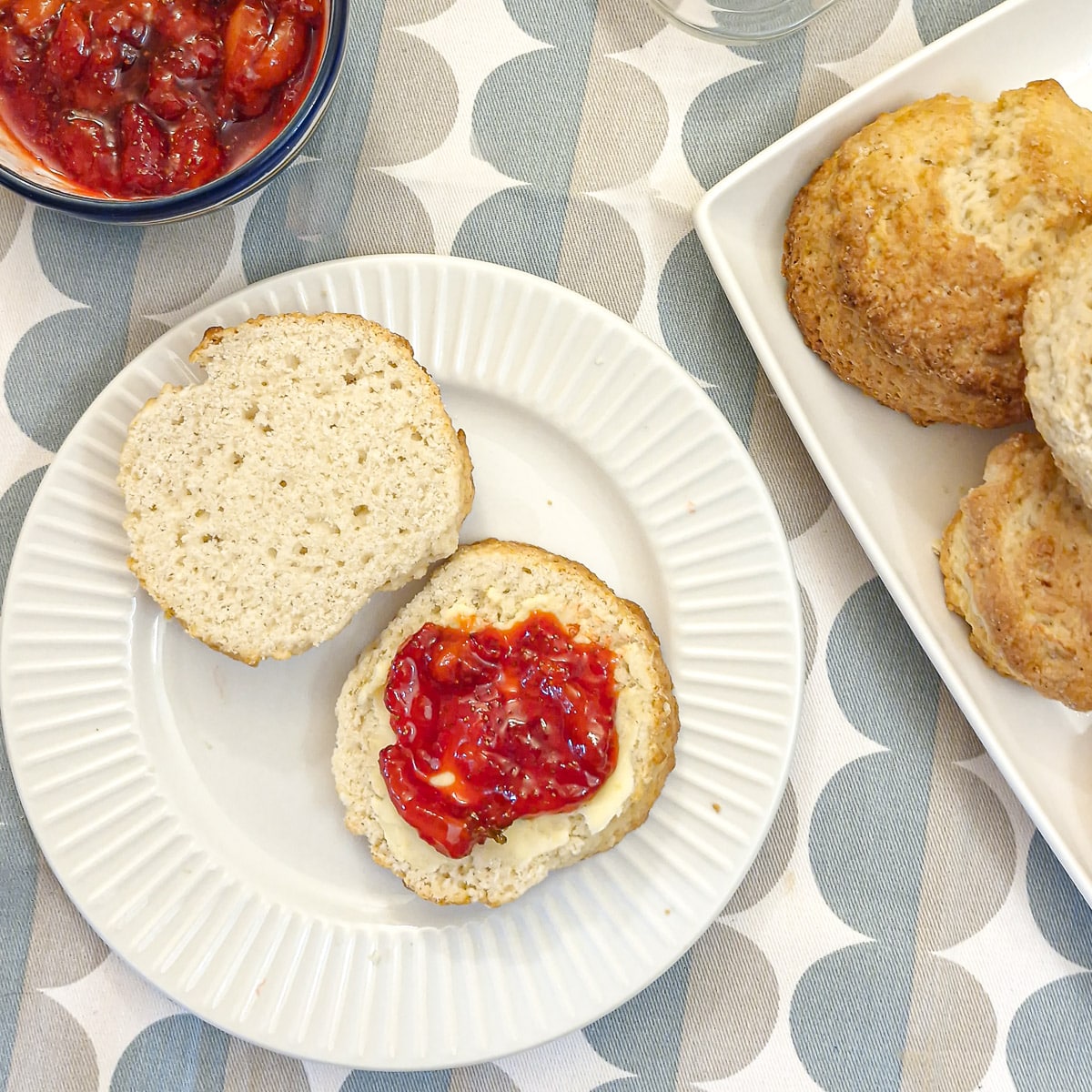 A cream scone cut in half, spread with butter and topped with strawberry compote.