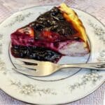 A slice of baked yoghurt cheesecake on a plate, topped with blueberry compote.