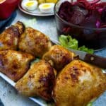 Pieces of air fried chicken on a white serving platter with bowls of salad in the background.