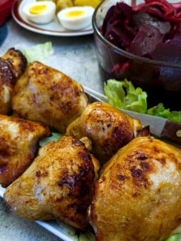 Pieces of air fried chicken on a white serving platter with bowls of salad in the background.