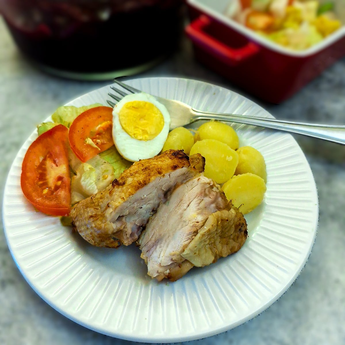 A piece of air fried chicken on a plate with salads, cut in half to show the inside.