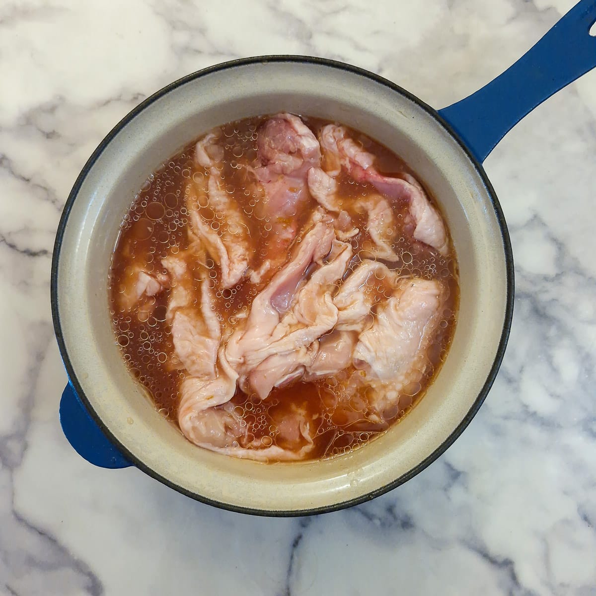 Pieces of chicken combined with marinade in a saucepan.