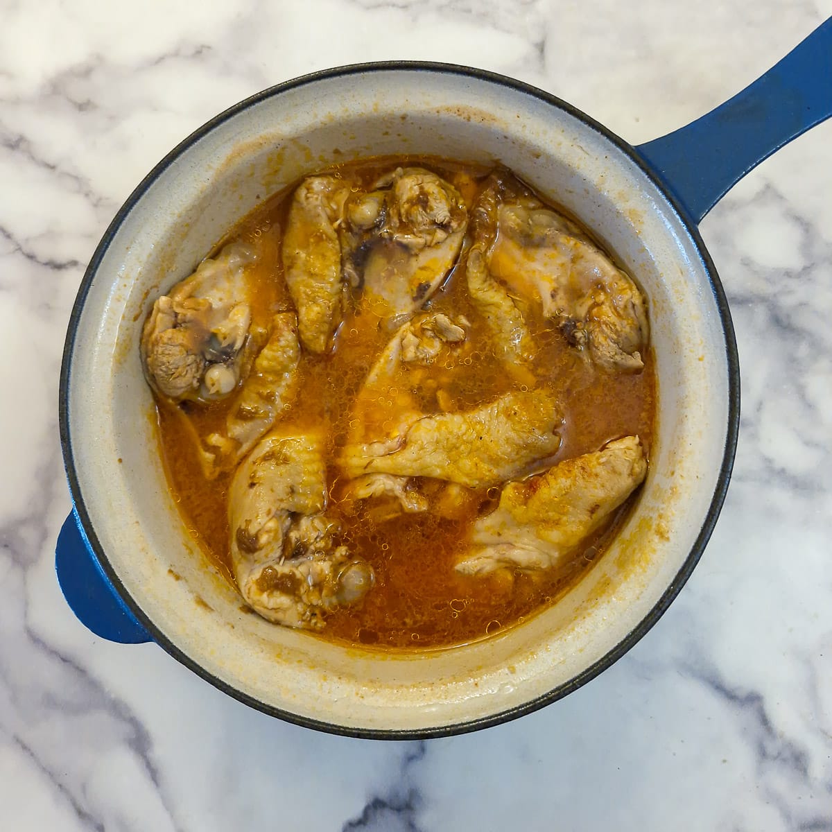 Chicken thighs that have been par-boiled in marinade in a saucepan.