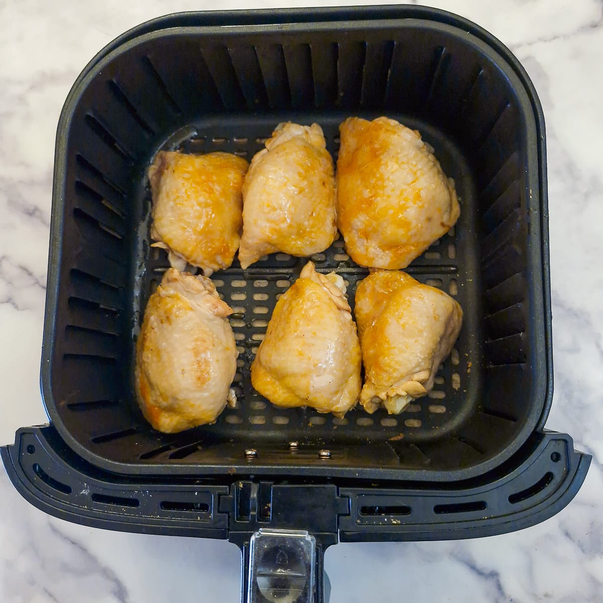 6 chicken thighs, skin side up, in an air fryer basket.