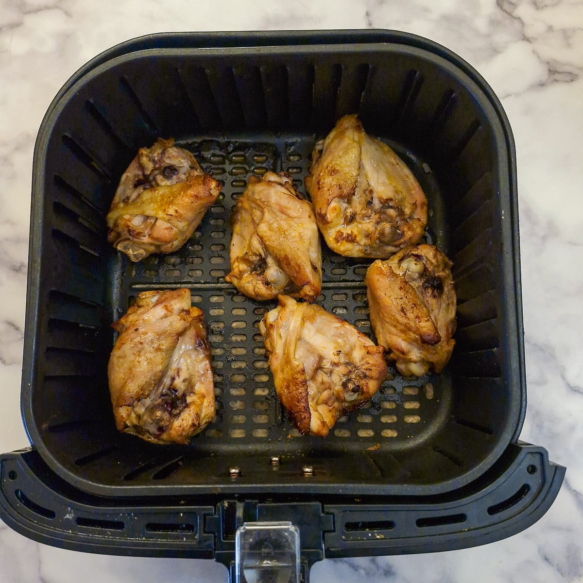 Chicken thighs in an air fryer basket turned over to cook the underneath.