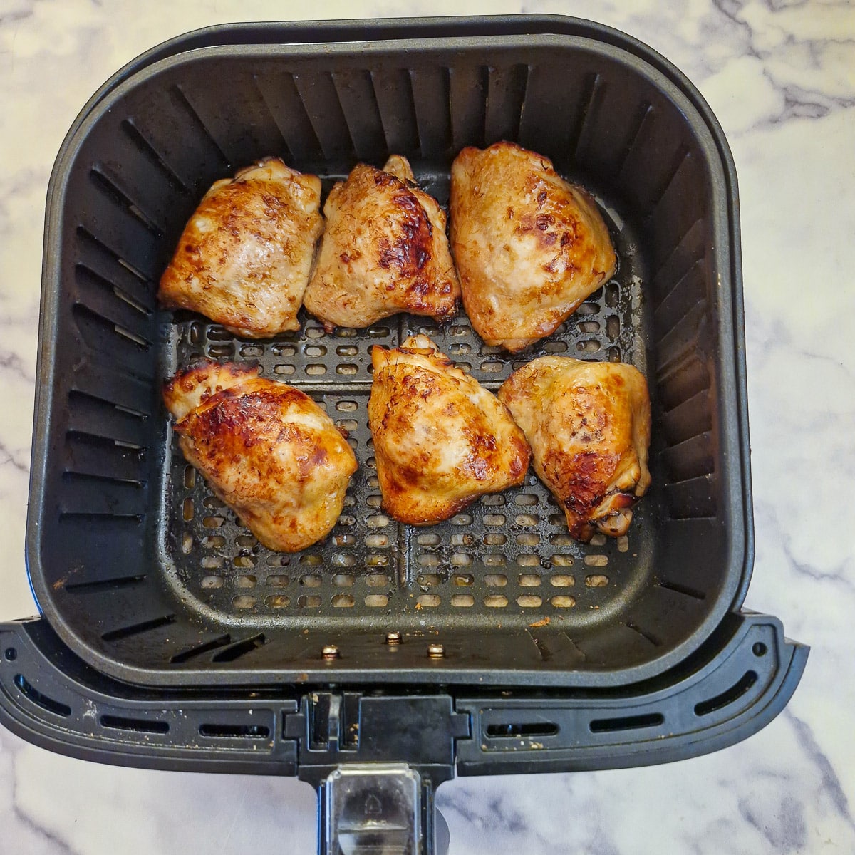 Compleetely browned chicken thighs in an air fryer basket.