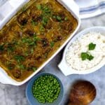 A dish of meatballs in curried onion sauce on a table next to a bowl of peas and a dish of rice.