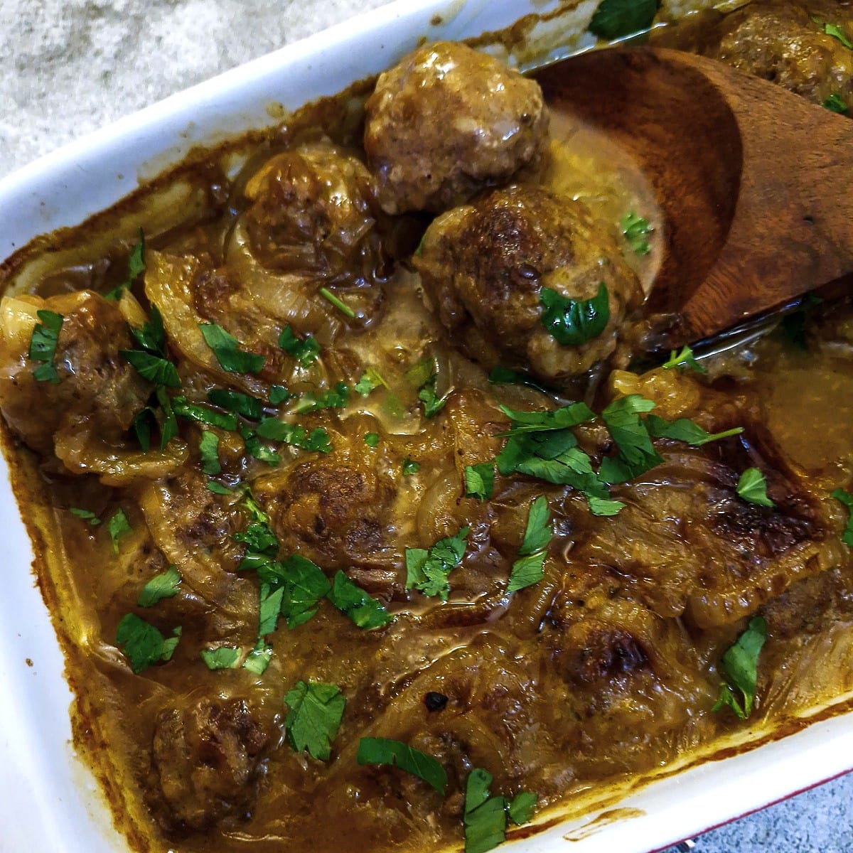 Overhead shot of curried meatballs in chutney and onion gravy in a casserole dish.