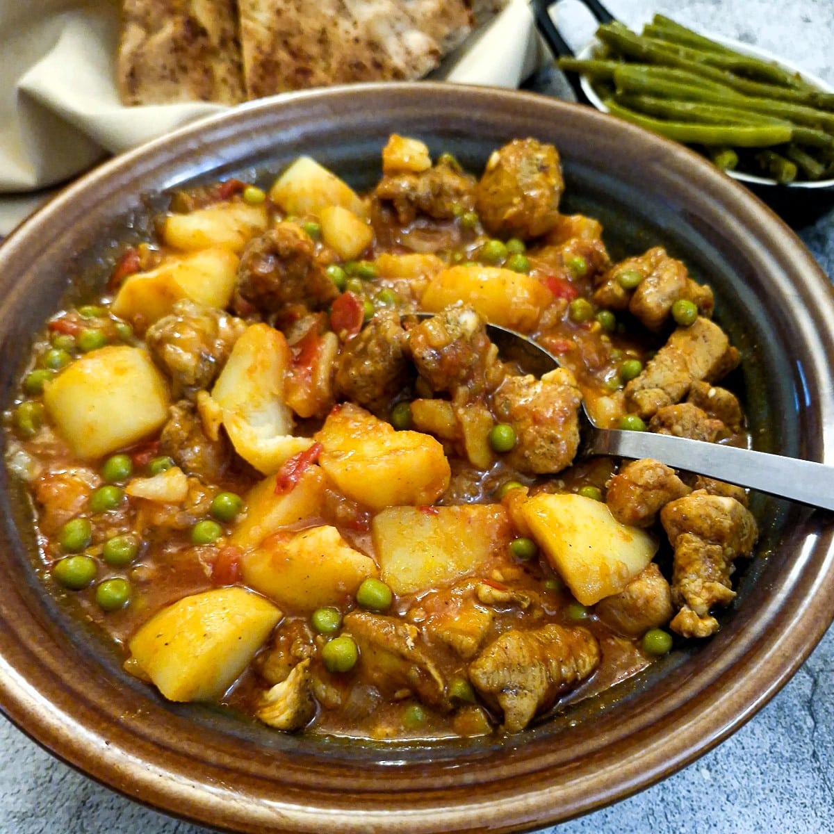 Close up of a dish of pea and potato curry with chicken pieces.