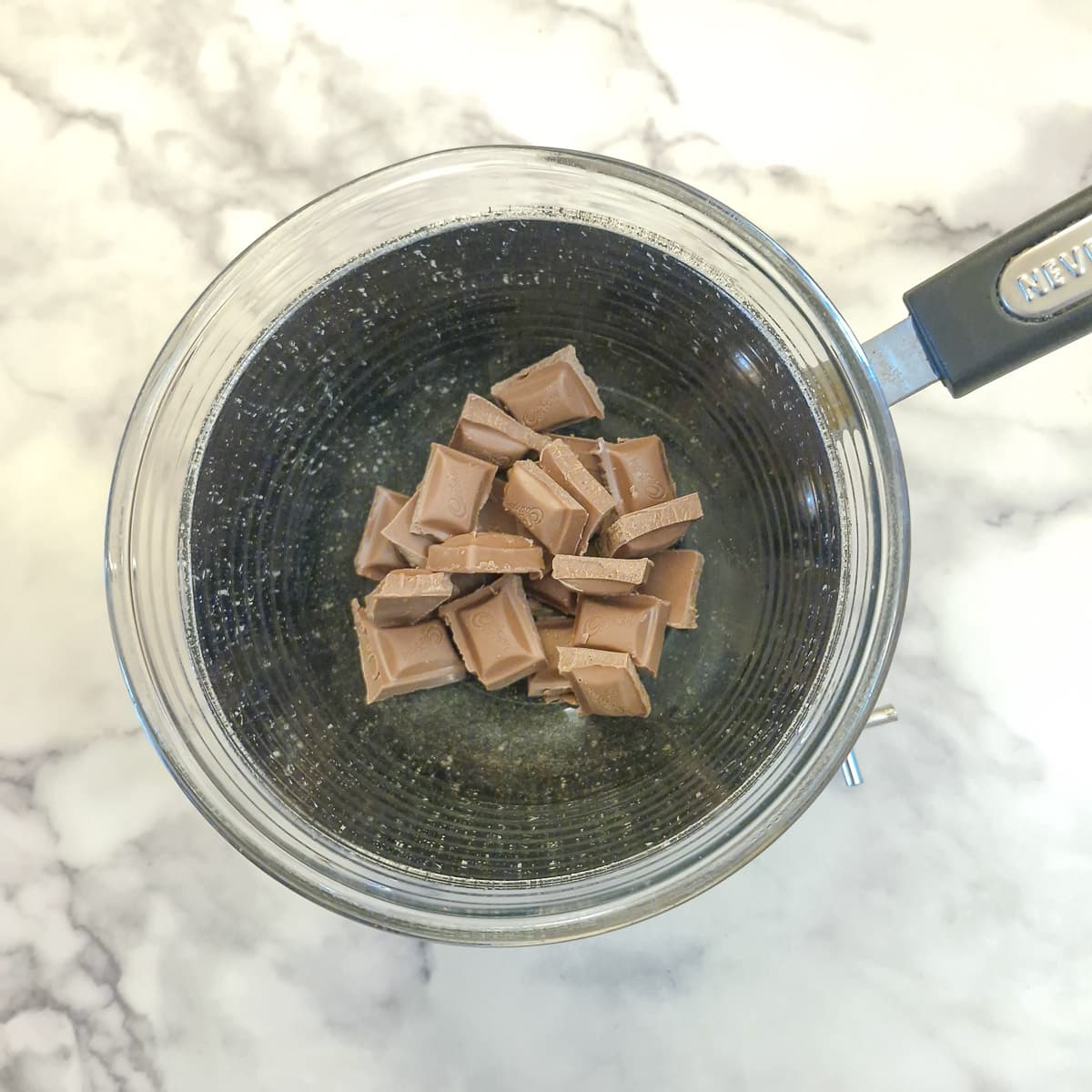 Step 5 - pieces of chocolate in a glass bowl over a saucepan.