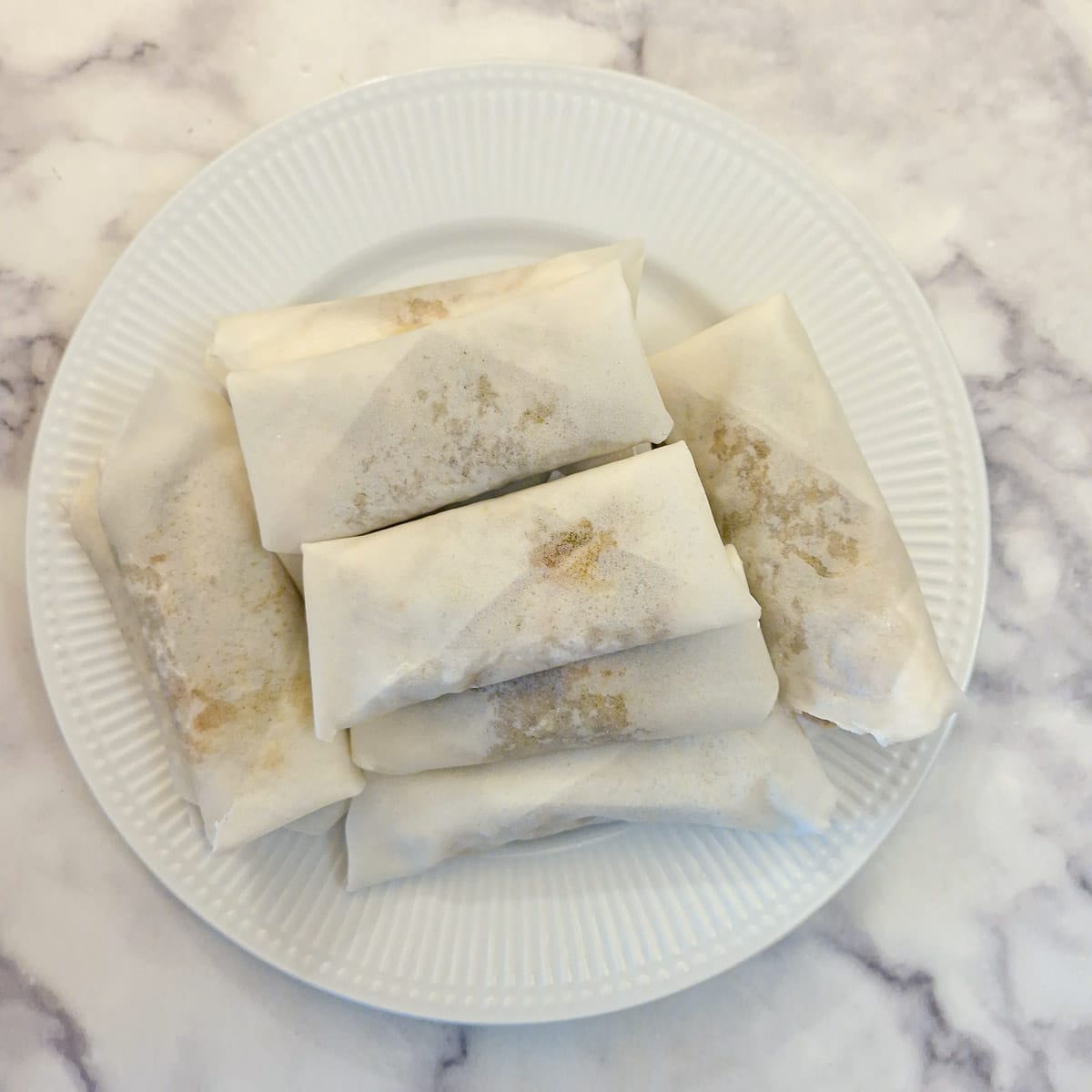 A pile of formed (unfried) spring rolls on a plate.
