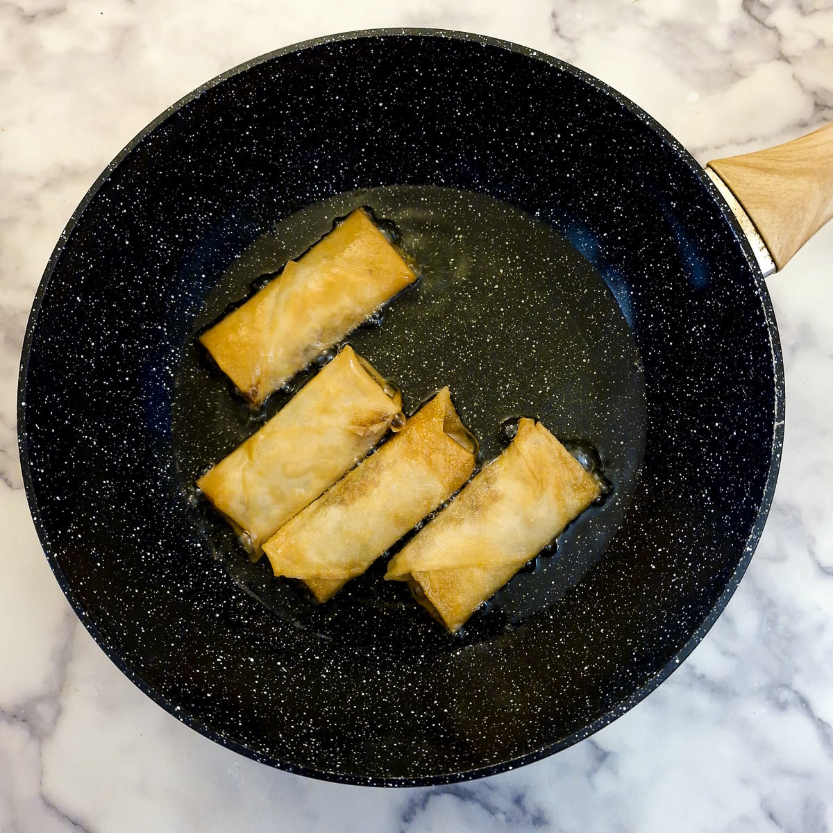 4 spring rolls browning in oil in a frying pan.