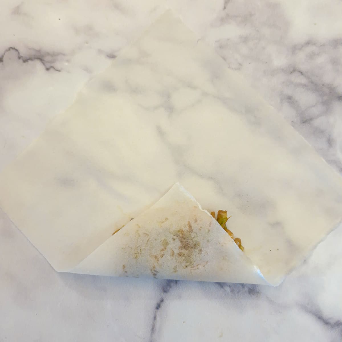 Step 6,  a corner of the spring roll wrapper folded over the filling.