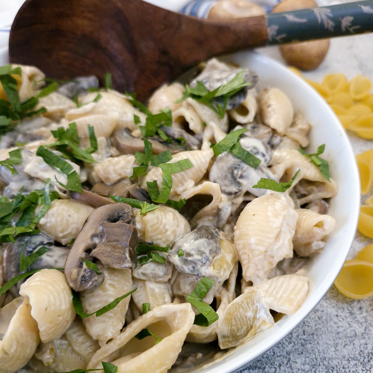 Close up of mushroom pasta salad in a serving dish with a  wooden serving spoon.