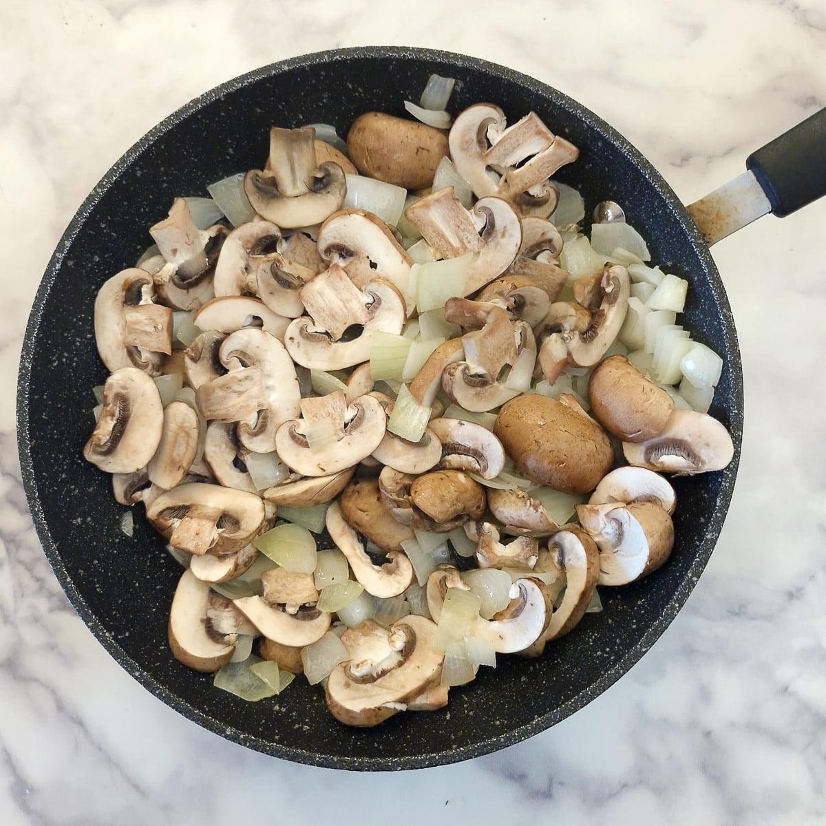 Mushrooms and onions in a frying pan.