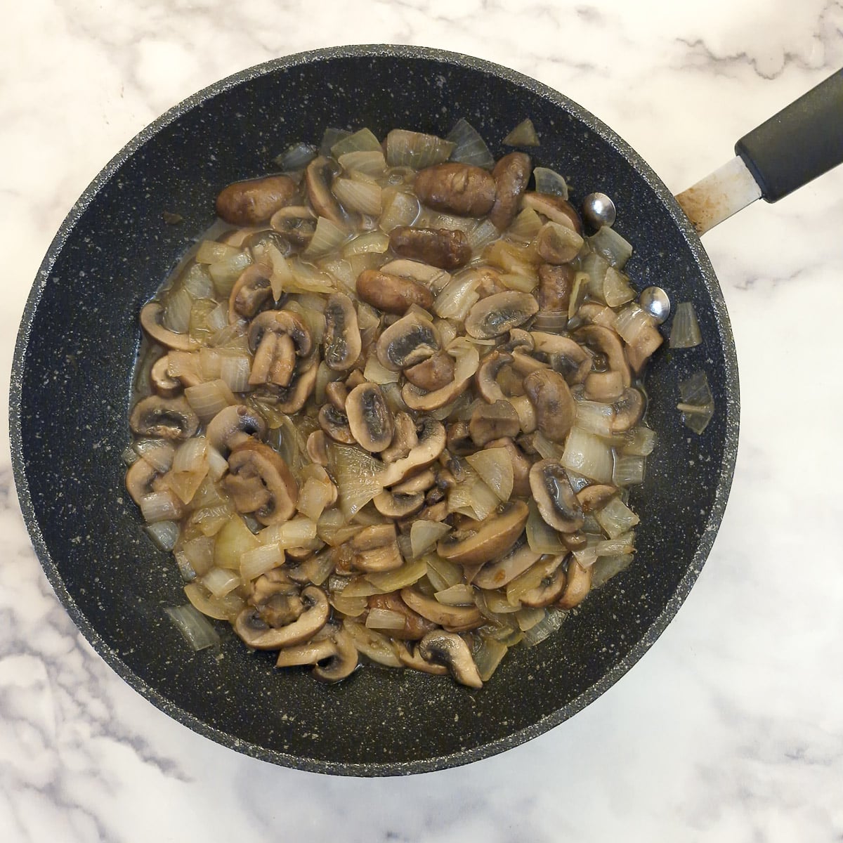 Fully cooked mushrooms and onions in a pan.