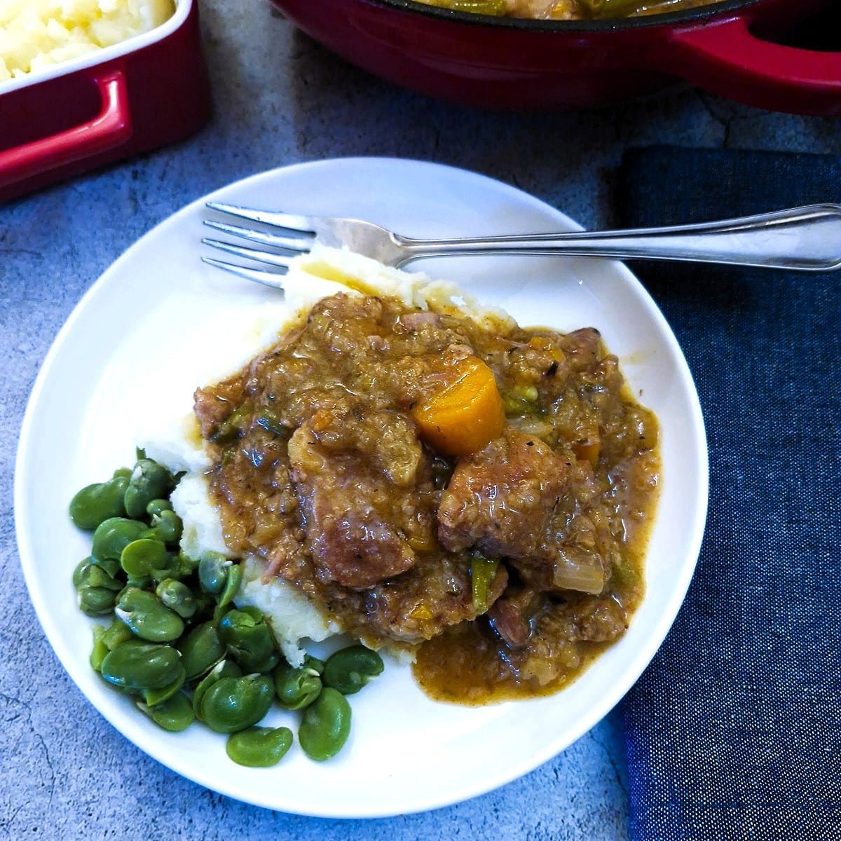 Pork and apple casserole  served over a pile of mashed potatoes on a white dinner plate.