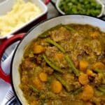A dish of pork and apple casserole on a table with mashed potatoes an broad beans.