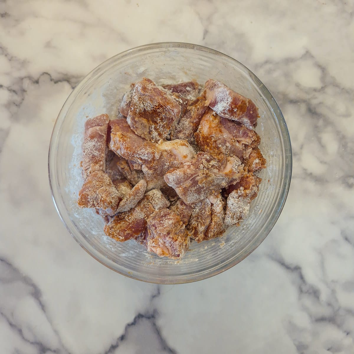 Pork pieces coated in seasoned flour in a glass bowl.