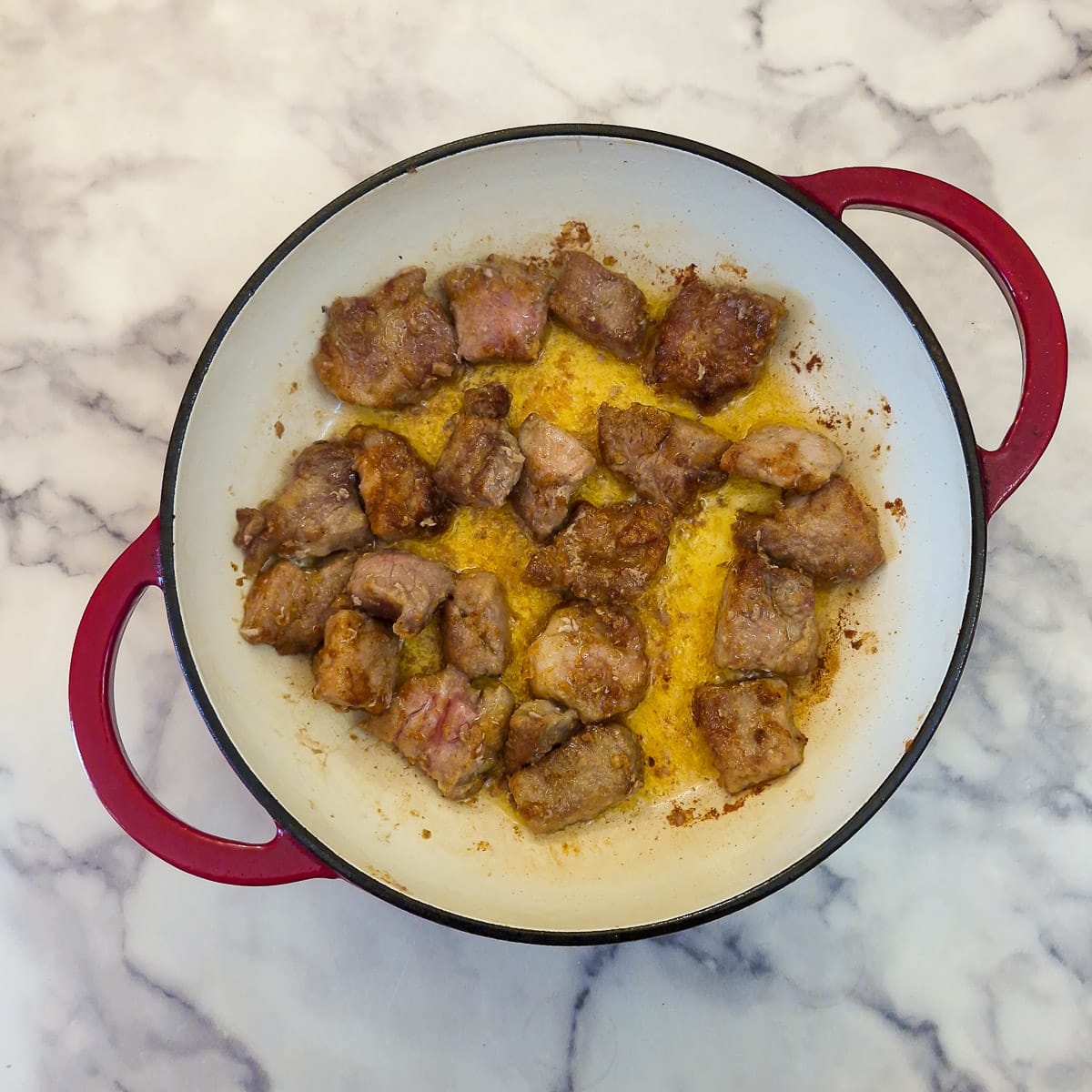 Seasoned pieces of pork browning in a casserole dish.